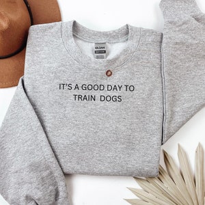 Könnte beinhalten: Grauer Pullover mit dem Aufdruck "It's a good day to train dogs" auf der Vorderseite.
