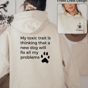 May include: A cream-colored hoodie with a black paw print and the text "My toxic trait is thinking that a new dog will fix all my problems".