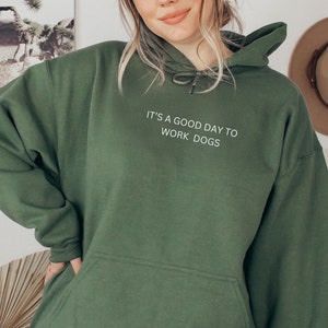 Könnte beinhalten: Ein dunkelgrüner Kapuzenpullover mit dem Aufdruck "It's a good day to work dogs" auf der Vorderseite.