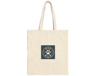 May include: A beige canvas tote bag with a dark blue square featuring a paw print and the text "DOG MOM" in a cream color.