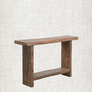 May include: A weathered wooden console table. The table has a rectangular top, supported by two upright legs and a lower shelf. The wood has a natural, aged appearance with visible grain and knots.