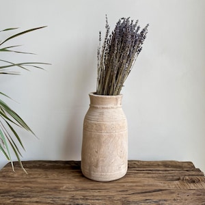 Könnte beinhalten: Eine hellfarbene Holzvase mit breitem Boden und schmalem Hals, gefüllt mit getrocknetem Lavendel. Die Vase steht auf einer rustikalen Holzoberfläche, mit einer Pflanze auf der linken Seite. Die Vase ist etwa 25 cm hoch.