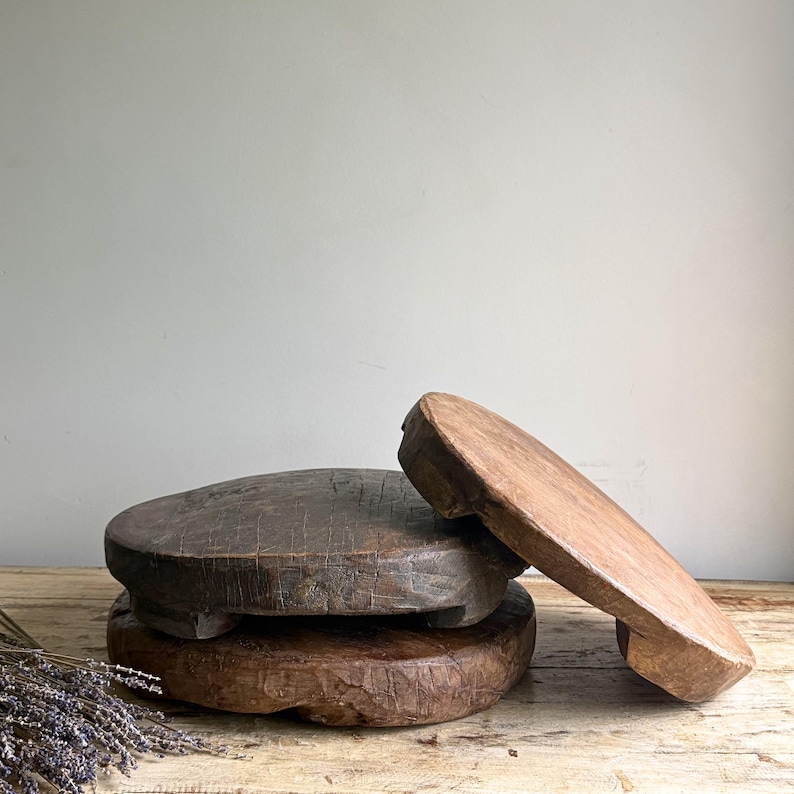 May include: Three circular wooden risers with a weathered, dark brown finish. The risers feature visible grain, natural cracks, and short, sturdy feet. Two are stacked horizontally, while the third is propped up against them at an angle.