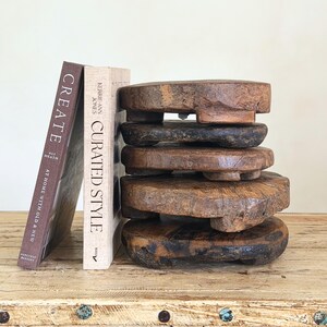 May include: A stack of five circular, weathered wooden risers with short feet, positioned next to two hardcover books titled Create: At Home with Old & New by Ali Heath and Curated Style by Kerrie-Ann Jones, featuring natural wood grain textures.