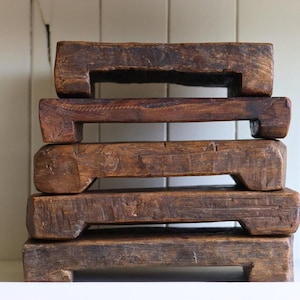 Könnte beinhalten: Ein Stapel aus fünf rechteckigen, rustikalen Holzständern. Jeder Ständer hat eine warme braune Farbe und an jedem Ende eine eingelassene Griffmulde. Die Holzmaserung ist sichtbar und trägt zur gealterten Ästhetik bei. Diese Ständer werden wahrscheinlich zur Präsentation oder Erhöhung verwendet.