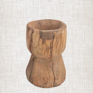 Könnte beinhalten: Ein zylindrischer Holzhocker oder Sockel, der aus einem einzigen Stück hellbraunem Holz geschnitzt wurde. Das Objekt weist eine verwitterte, strukturierte Oberfläche mit sichtbarer natürlicher Maserung, tiefen Rissen und einer Vertiefung auf.