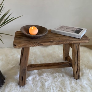 Puede incluir: Mesa auxiliar rústica de madera con acabado envejecido. Una vela naranja encendida está en un cuenco marrón oscuro. Un libro titulado "The Modern Apothecary" descansa sobre la mesa. La mesa mide aproximadamente 61 cm de largo.