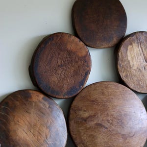 May include: A collection of circular wooden boards with a dark brown finish and visible grain patterns. The boards vary in size and texture, with some featuring weathered surfaces and small feet, arranged in a cluster against a plain background.