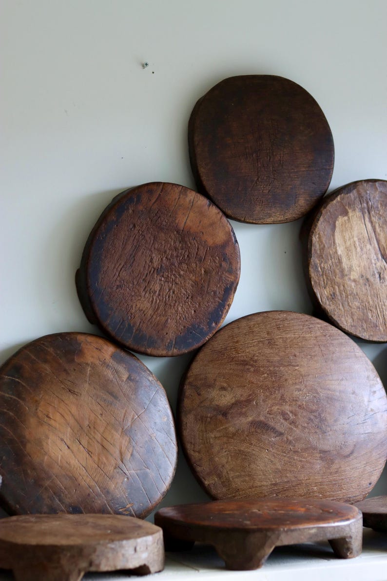 May include: A collection of circular wooden boards with a dark brown finish and visible grain patterns. The boards vary in size and texture, with some featuring weathered surfaces and small feet, arranged in a cluster against a plain background.