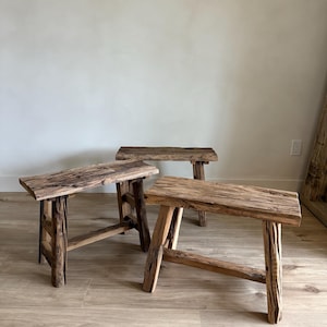 Könnte beinhalten: Drei rustikale Holzstühle mit natürlicher Holzmaserung. Jeder Hocker hat eine rechteckige Sitzfläche und vier stabile Beine, die die rohe Schönheit des Holzes zeigen. Die Hocker sind auf einem hellen Holzboden angeordnet.