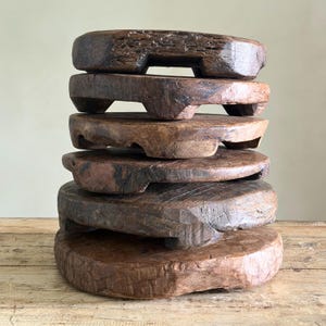 May include: A stack of six circular wooden risers, each featuring a dark brown, weathered finish with visible grain patterns and textures. Every piece is supported by three short, integrated feet, creating a tiered display of rustic, solid wood platforms.