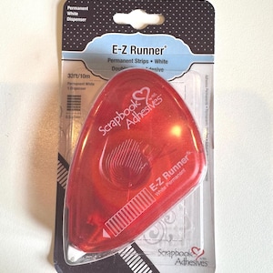 May include: A red E-Z Runner permanent adhesive dispenser for scrapbooking. The package includes 33 feet of white adhesive strips. The package has the text "Scrapbook Adhesives" and "E-Z Runner".