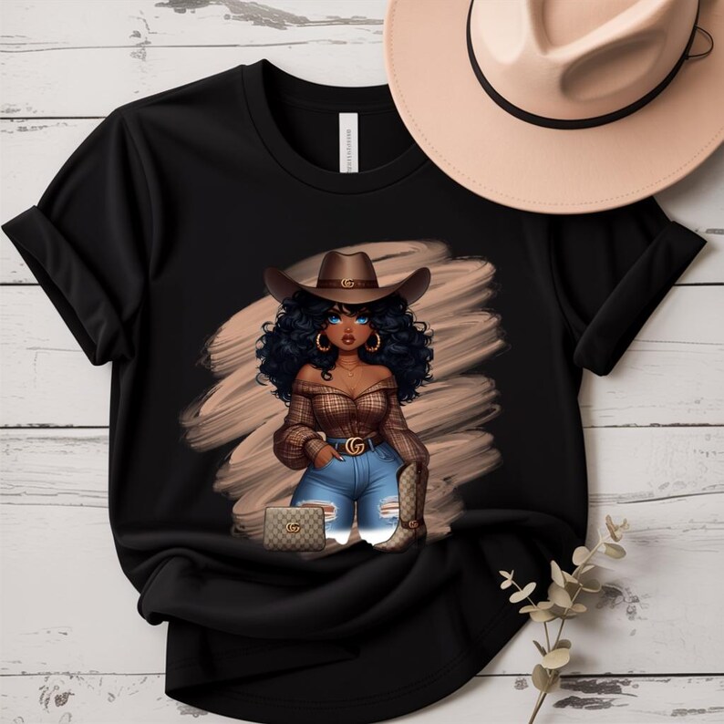 May include: Black t-shirt featuring a graphic of a cowgirl with blue eyes, curly black hair, and a brown cowboy hat. The cowgirl is wearing a plaid top, blue jeans, and cowboy boots. A beige cowboy hat rests on the top right.