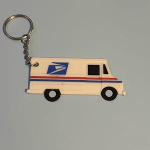 May include: A white USPS mail truck keychain with a blue and red stripe design. The keychain features a silver chain and ring. The mail truck has black wheels and windows, and a blue USPS logo.