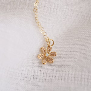 Peut inclure: Un collier en cha&icirc;ne dor&eacute;e avec un petit pendentif en forme de fleur scintillante. La fleur a un centre blanc et est entour&eacute;e de strass transparents.