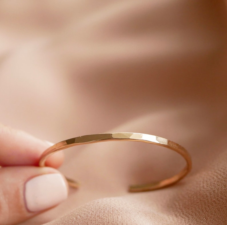 May include: A gold hammered bangle bracelet. The bracelet is simple and delicate, with a smooth, polished finish.