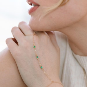 May include: A gold chain bracelet with four small green gemstones. The bracelet is designed to be worn around the wrist and up the hand, with the chain extending to the fingers.