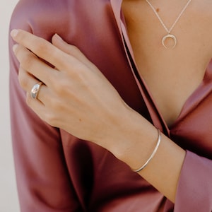 May include: A silver ring with a rounded, smooth design, a silver bracelet with a simple, curved shape, and a silver necklace with a crescent moon pendant.