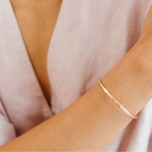 May include: A simple gold bangle bracelet on a person's wrist.