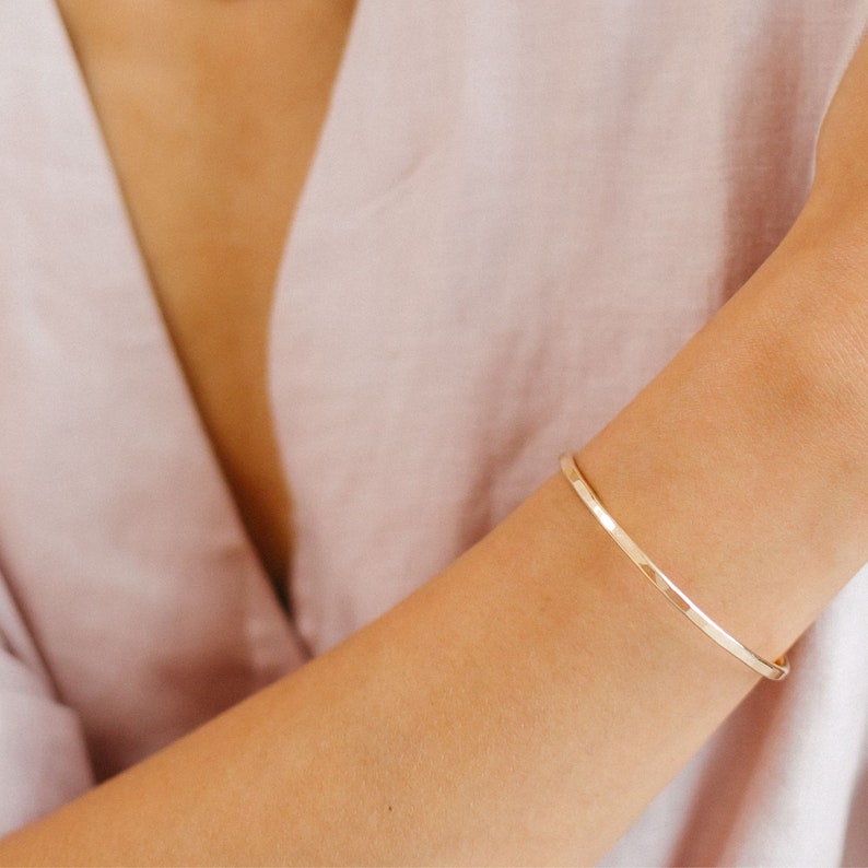 May include: A simple gold bangle bracelet on a person's wrist.