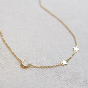 May include: A gold chain necklace with a crescent moon charm and three star charms.