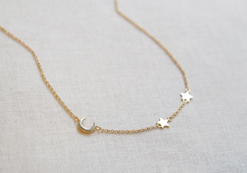 May include: A gold chain necklace with a crescent moon charm and three star charms.