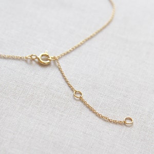 May include: A gold chain necklace with a lobster clasp and an extender chain. The chain is made of small, delicate links.