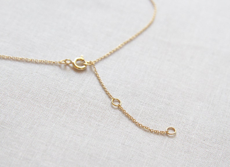 May include: A gold chain necklace with a lobster clasp and an extender chain. The chain is made of small, delicate links.