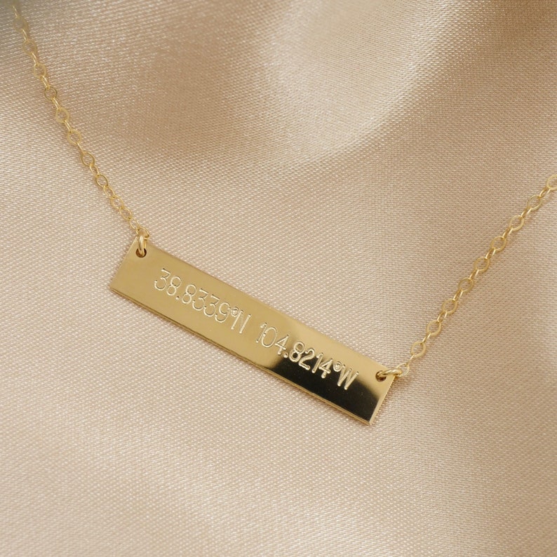 K&ouml;nnte beinhalten: Goldkette mit einem Barren-Anh&auml;nger, der mit den Koordinaten 39.833911 104.8214&deg;W graviert ist.