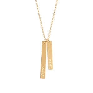 May include: A gold-colored necklace with two rectangular pendants. One pendant reads "MAMA," and the other reads "JAMES." The pendants hang from a delicate gold chain, creating a simple and elegant design.