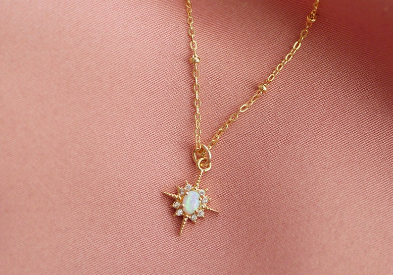 May include: A gold chain necklace with a star-shaped pendant featuring a white opal stone surrounded by smaller clear stones.