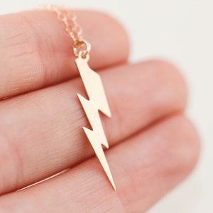 May include: A gold lightning bolt pendant necklace. The pendant is a simple, stylized design of a lightning bolt.