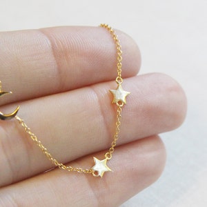 May include: A delicate gold chain necklace with a crescent moon charm and two star charms.