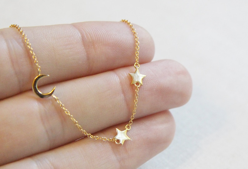 May include: A delicate gold chain necklace with a crescent moon charm and two star charms.