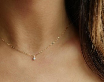 May include: A delicate gold chain necklace with a small, clear gemstone pendant.