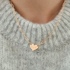 May include: A gold chain necklace with a heart-shaped pendant engraved with the letters "SAE".