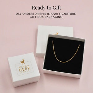 May include: A white gift box with a gold deer logo that says "Amanda Deer Jewelry". The box is open and a gold chain necklace is inside.