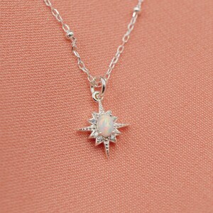 May include: A silver necklace with a starburst pendant featuring a white opal gemstone. The necklace has a delicate chain with small silver beads.