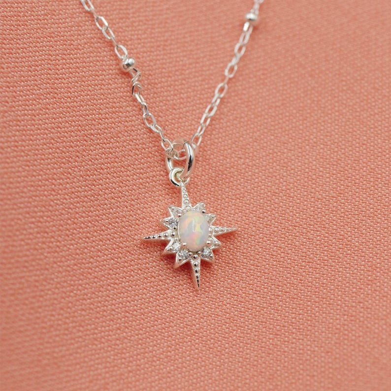 May include: A silver necklace with a starburst pendant featuring a white opal gemstone. The necklace has a delicate chain with small silver beads.