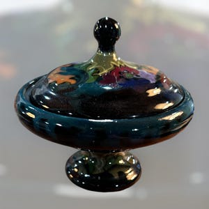 Könnte beinhalten: Eine Keramik-Servierplatte mit Deckel. Die Platte ist mit bunten Blumenmustern verziert und hat eine glänzende Oberfläche. Der Deckel hat einen Knopf oben.