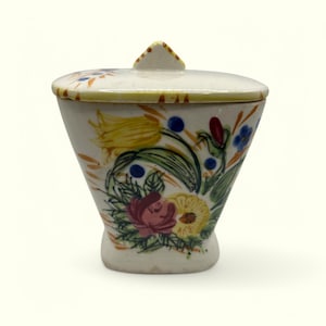 May include: A white ceramic sugar bowl with a lid, featuring a floral design with yellow, red, blue, and green flowers. The bowl has a rounded base and a slightly flared top.