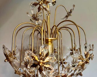 May include: A gold chandelier with crystal flower accents. The chandelier has a round shape and is made of metal.
