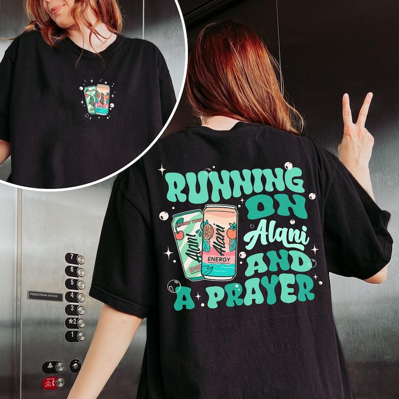 May include: Black t-shirt with a graphic of two energy drink cans and the text "Running on Alani and a Prayer" in green and white. The shirt has a small graphic on the front and a larger design on the back.