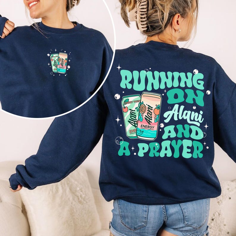 May include: Navy blue sweatshirt with a graphic of two energy drink cans and the text "Running on Alani and a Prayer" in teal and white. The front of the sweatshirt has a smaller version of the can graphic.