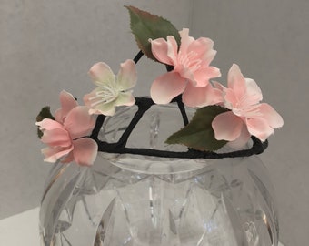 May include: A black wire hair comb with pink and white silk flowers attached. The comb is sitting in a clear glass vase.