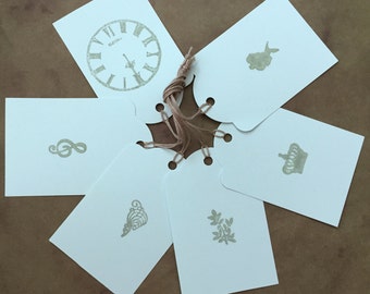 May include: Six white gift tags with different designs, including a clock, a musical note, a crown, a mermaid, a heart, and a leaf. The tags are tied together with twine.