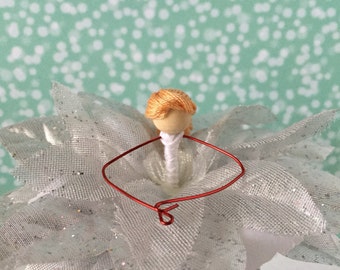May include: A white, glittery flower with a red wire frame. A small doll with orange hair and a white dress is sitting in the center of the flower.