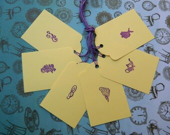 May include: Six yellow gift tags with purple ink designs. The designs include a teapot, a flower, a swirl, a bird, a teapot, and a swirl.