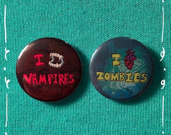 May include: Two circular badges with the text "I Vampires" and "I Zombies". The "I" is a heart shape. The vampire badge is dark red with white teeth. The zombie badge is blue with a red heart.