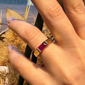 May include: A gold ring with a rectangular red stone set in the band.